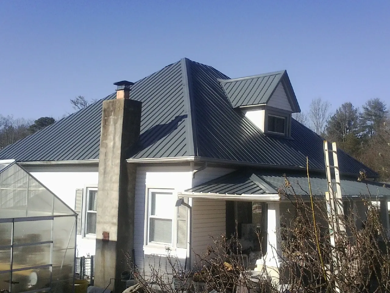 Dark blue standing seam metal roof on a white farmhouse with dormer — Slate & Tile Roof Repair by Roofing Brothers in Chapman