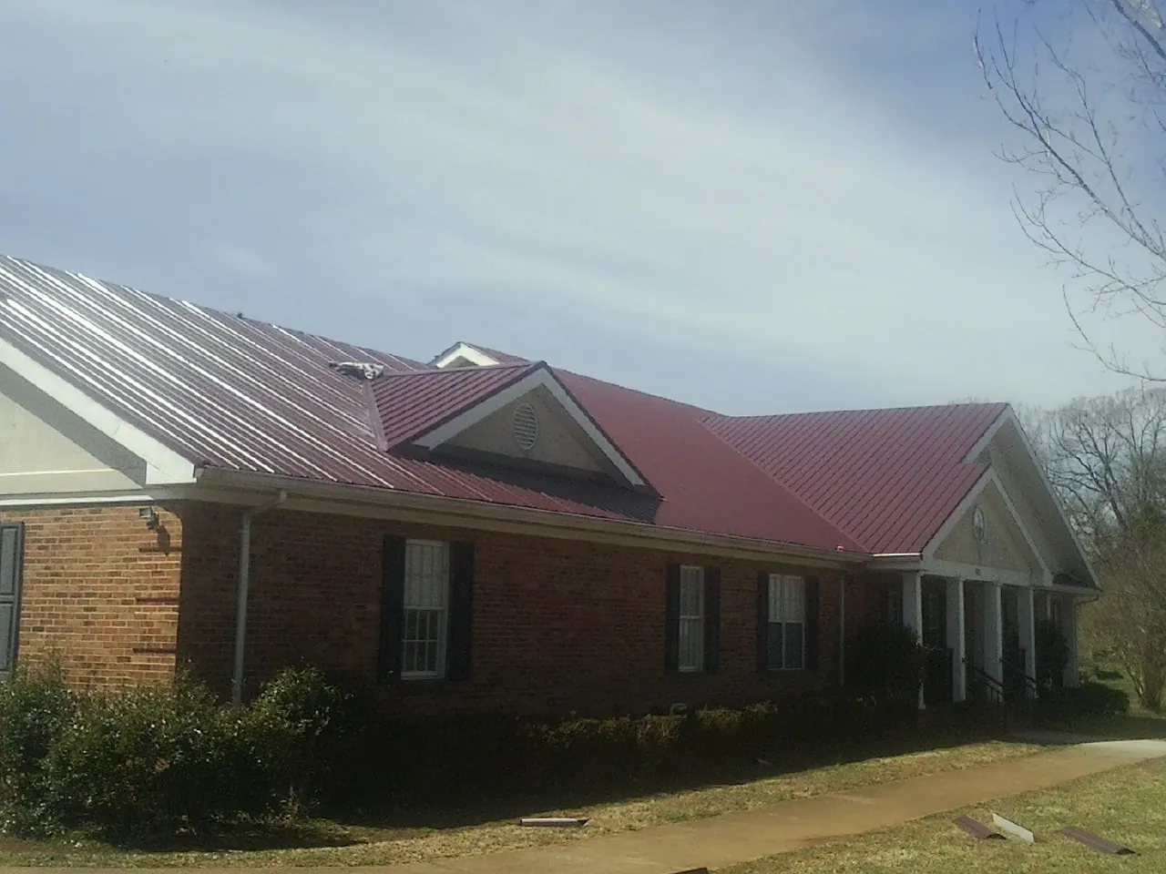 Red metal roof with gabled entries on a long brick building, from a Hail Damage Roof Repair job in Chapman
