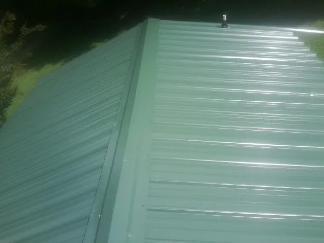 New green metal panels meeting at the ridge of a roof — Flat Roof Repair work by our crew in Chapman