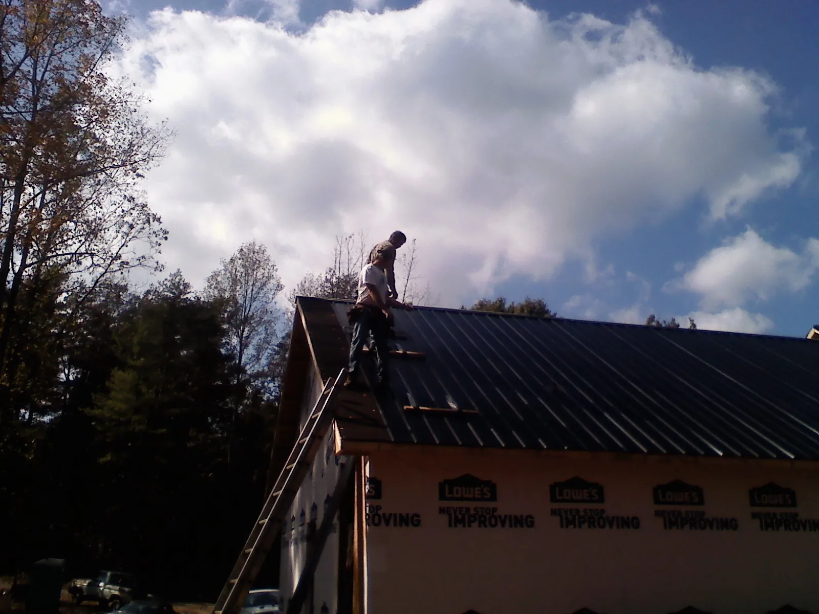 Roofer fastening dark metal panels high against a cloudy sky, from a Roof Inspection job in Chapman